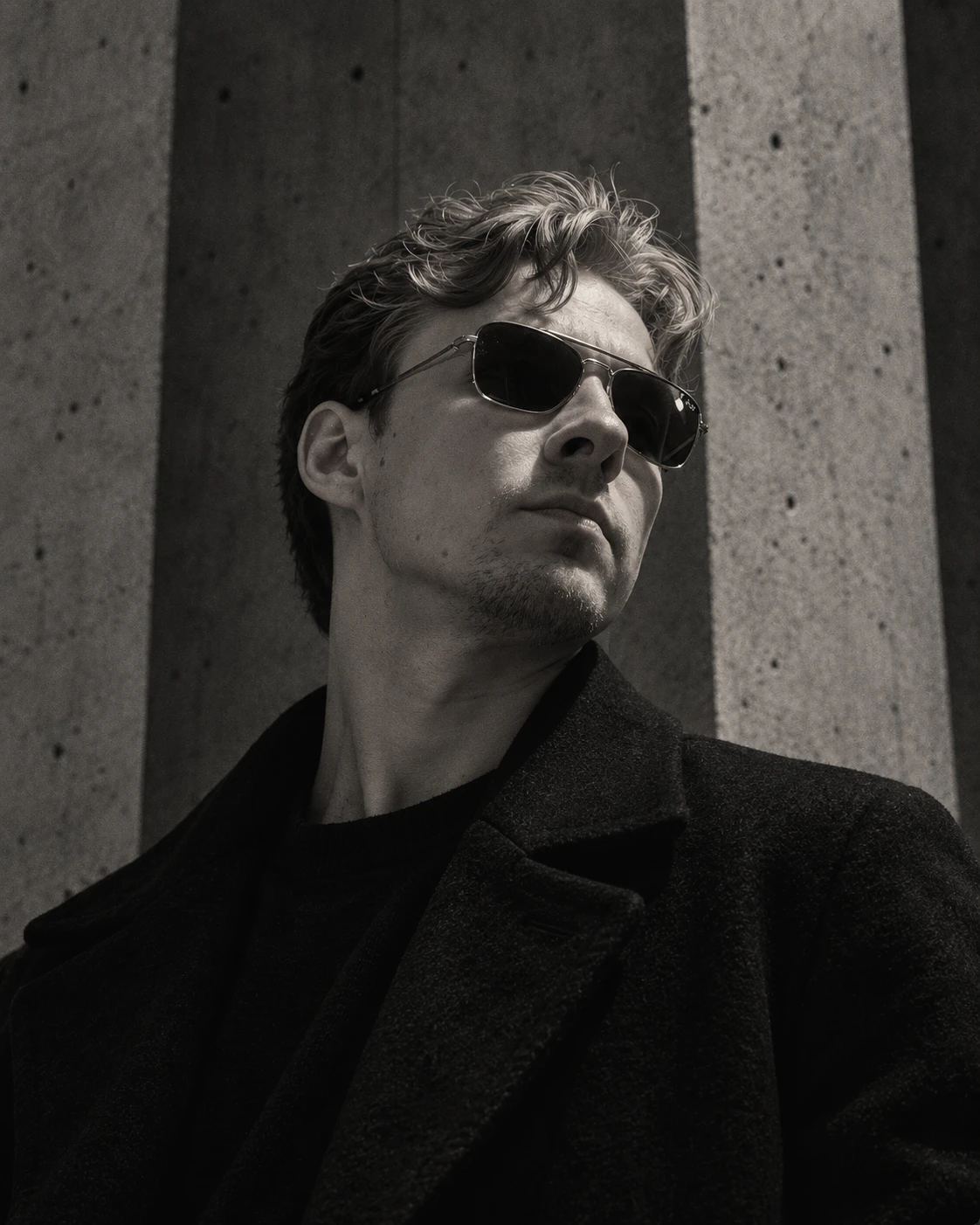 Monochrome portrait in a brutalist architectural setting.